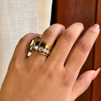 Hand wearing a gold ring with gemstones against a neutral background