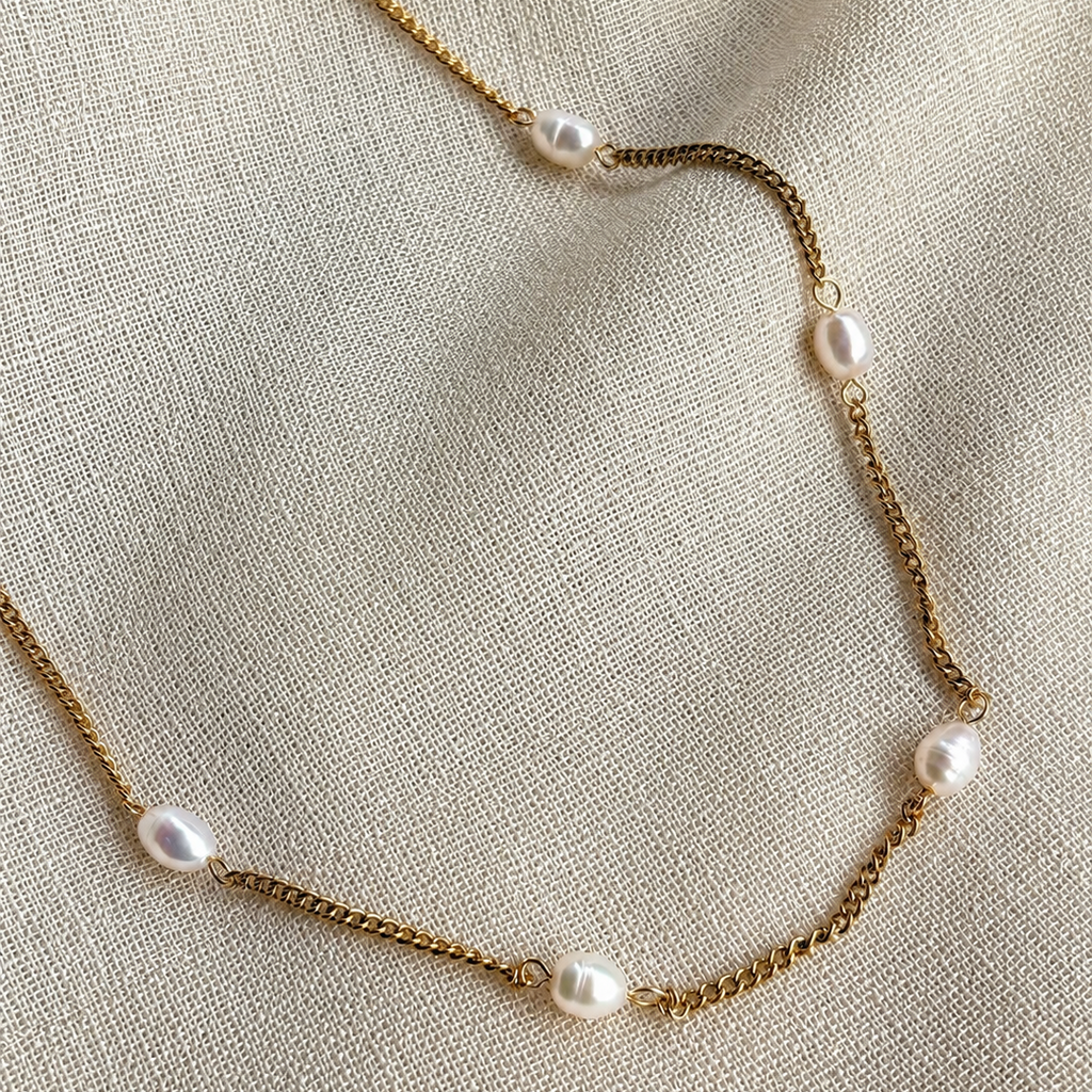 Gold necklace with pearls on a beige fabric background