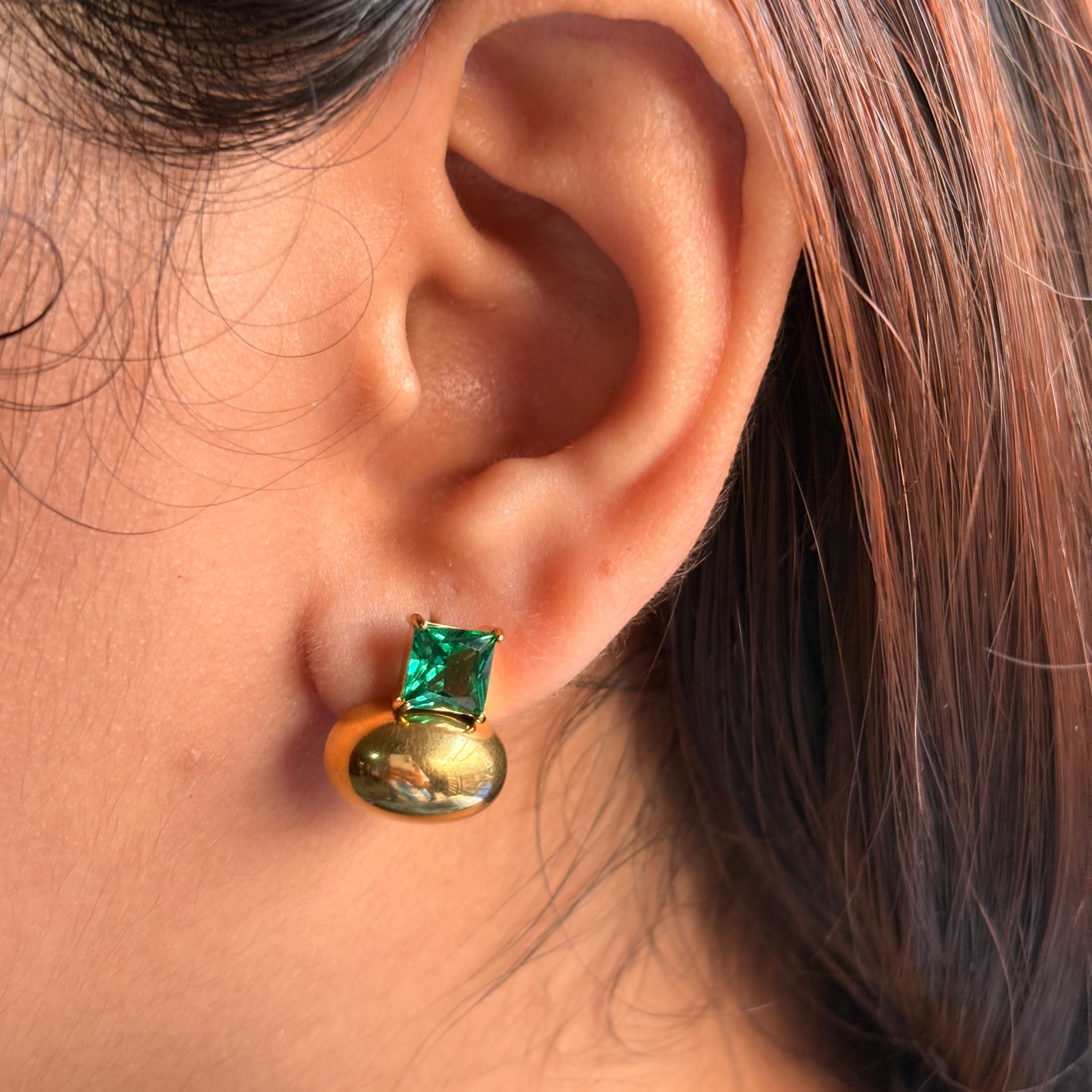Close-up of an ear wearing a gold earring with a green gemstone.