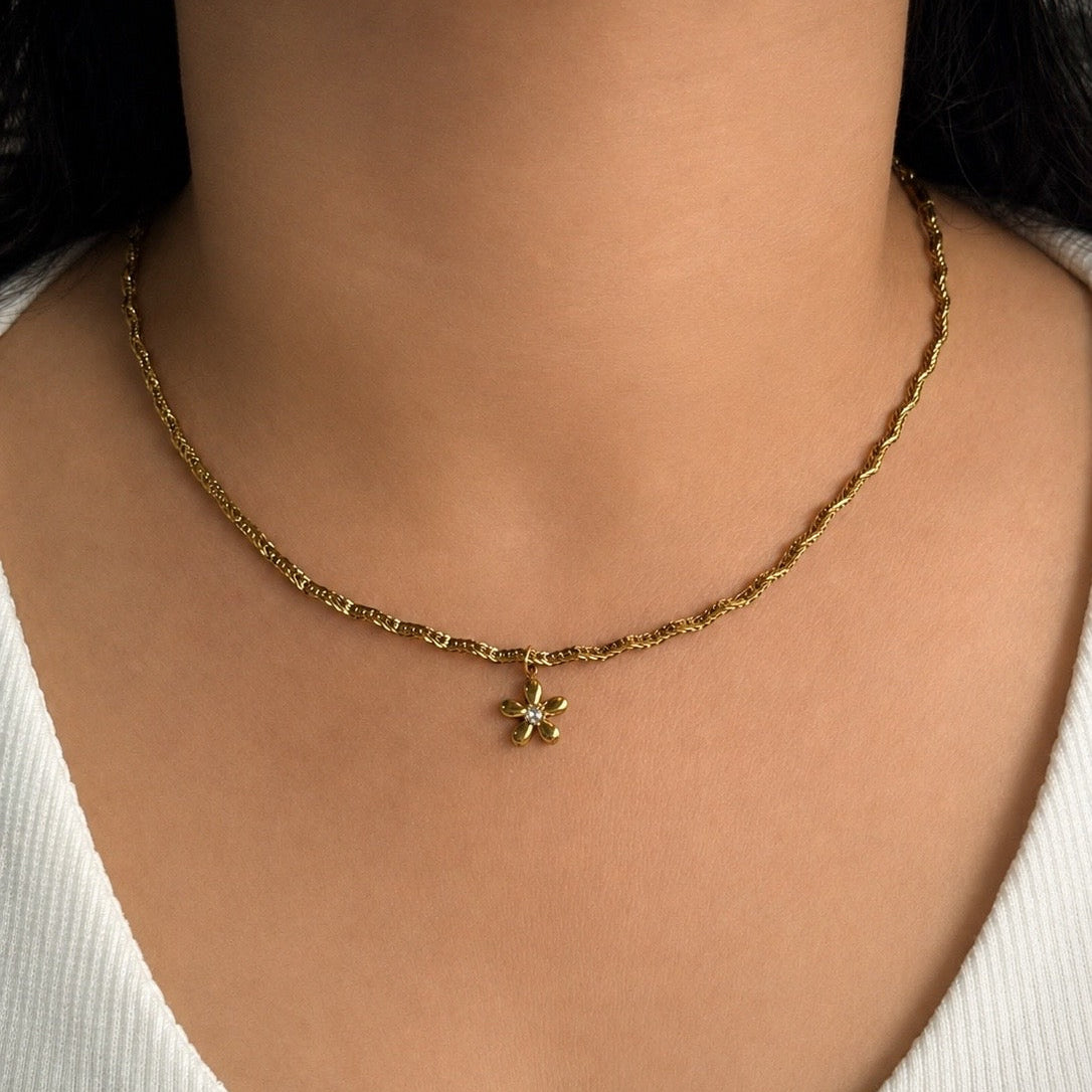 Gold necklace with a clover pendant on a person wearing a white top.