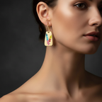 Pretty Shimmering Things Global Aurora gold-tone drop earrings featuring a vibrant multi-colored leaf motif on a model