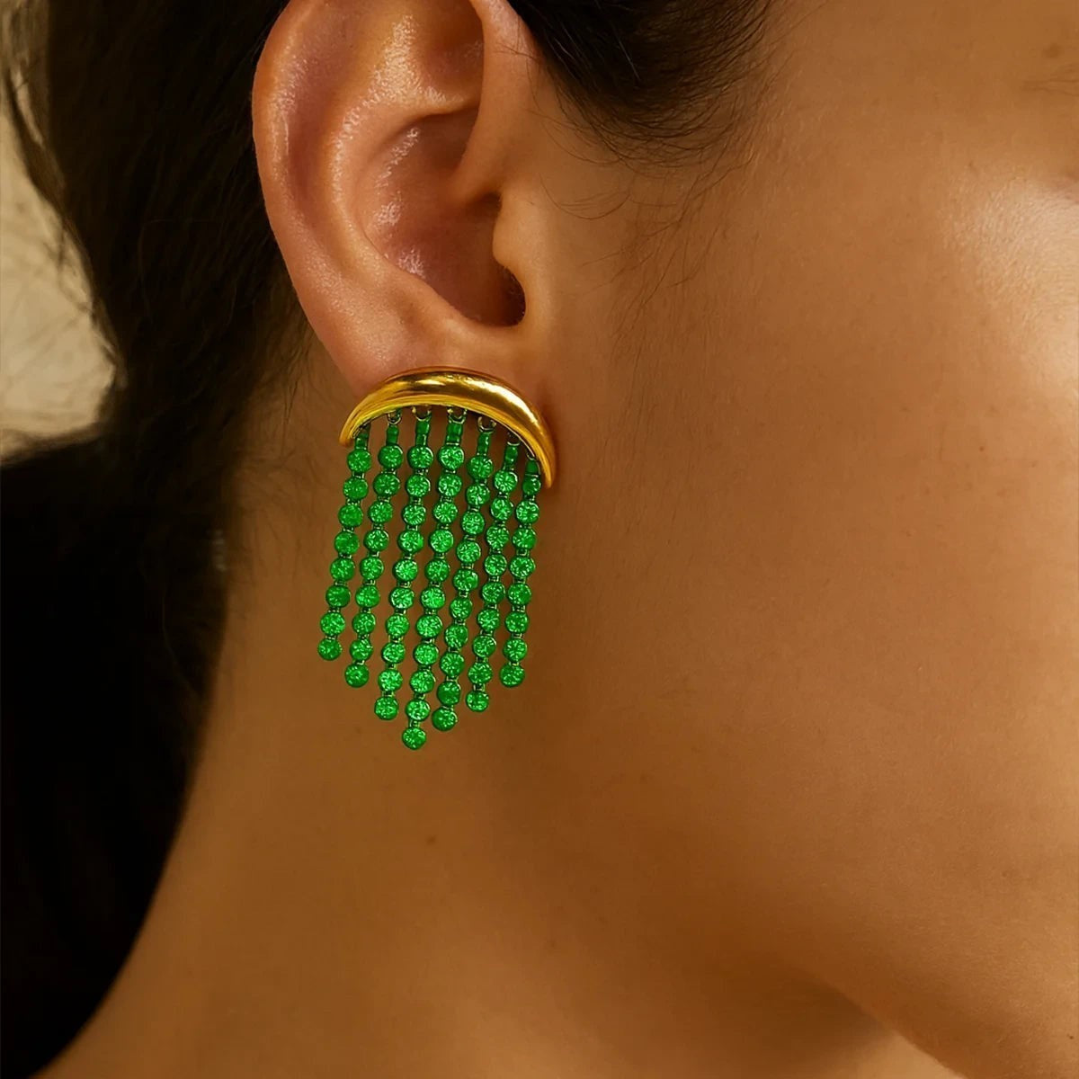 Pretty Shimmering Things Global gold crescent fringe earrings with cascading emerald green crystal strands on a model