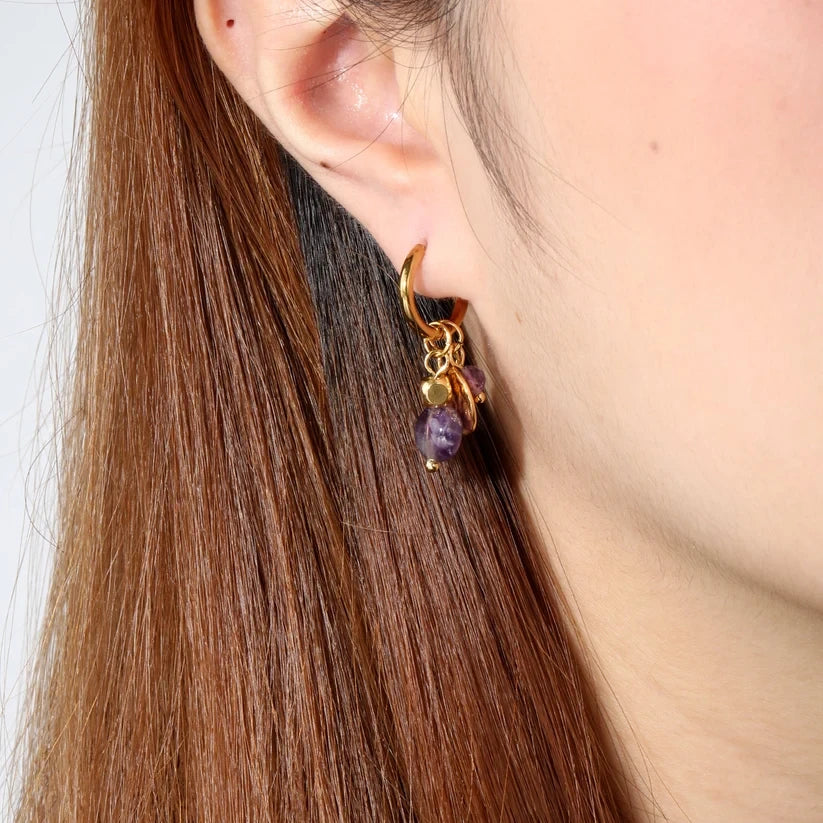 Pretty Shimmering Things Global gold hoop earrings with purple amethyst-inspired charms worn on a model's ear