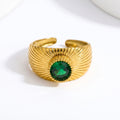 Pretty Shimmering Things gold-tone sunburst statement ring with a deep emerald-green gemstone and adjustable open band.